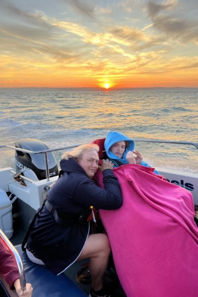 Mother and daughter (in wheelchair) on boat with sunset behind them